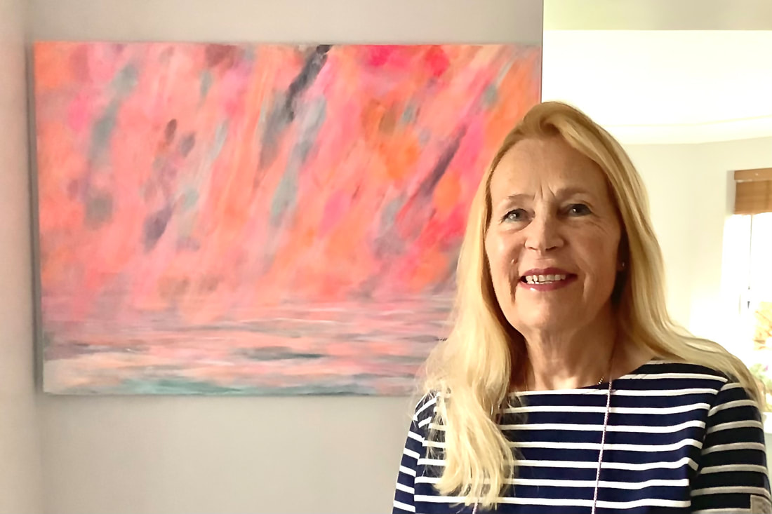 Esther Marshall Artist | a portrait of a blonde woman standing in front of an abstract painting. The painting is primarily comprised of warm pink hues.